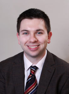 business headshot of a law student in dark jacket and tie looking at the camera smiling