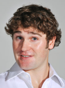 actor headshot of a man with white shirt and a curious look