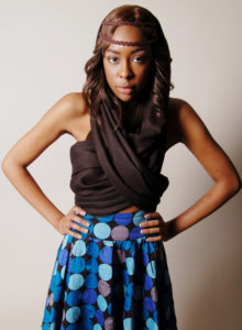 model in dark blouse and blue dotted skirt with her hands on her hips looking at the camera