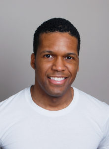 actor's headshot of a black man in white t-shirt with a broad smile