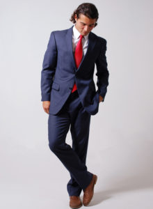 picture of a male model in blue suit and red tie standing looking down
