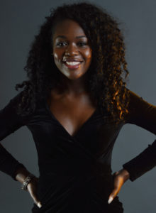 black model with curly hair wearing a black dress with hands on waist