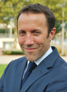 casual business headshot of a man in suit with a sneaky smile