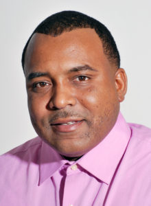 actor's headshot of a black man in light pink shirt