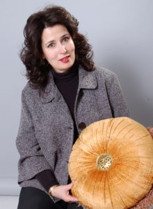 promotional headshot of an interior designer in dark grey jacket showing a decorative pillow