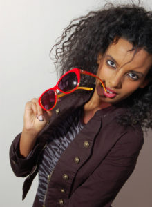 picture of a model with curly hair holding glasses close to her face