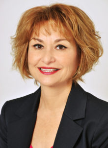 business headshot of a executive woman in dark navy suit and scarlet blouse smiling